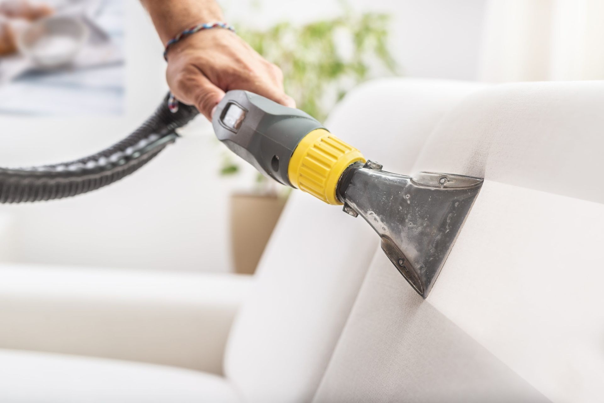 Person using a vacuum cleaner attachment to clean a white sofa.